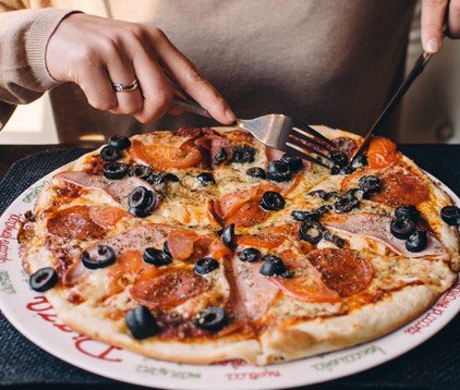 Persona taglia una pizza con olive e salame.
