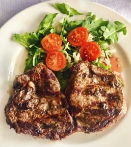 Bistecche con rucola e pomodorini su piatto bianco.