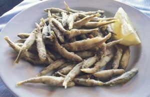 Pesciolini fritti su piatto con fetta di limone.
