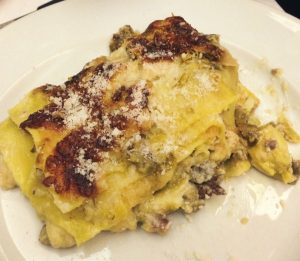 Lasagna su piatto bianco con formaggio grattugiato.