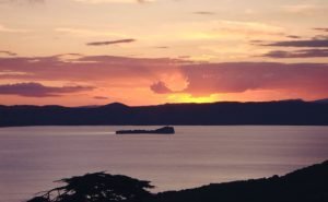 Tramonto su lago con isola e cielo colorato.