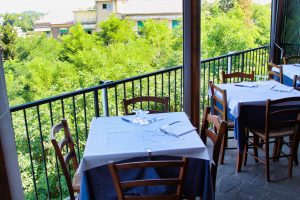 Tavoli apparecchiati su terrazza con vista alberi.