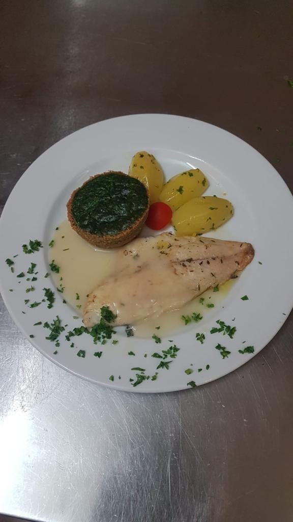 Piatto con pesce, spinaci, patate e pomodoro.