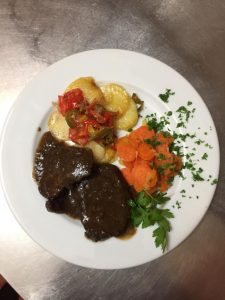 Piatto con carne, patate, carote e prezzemolo.