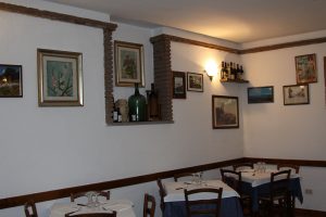 Interno di ristorante con tavoli apparecchiati e quadri alle pareti.