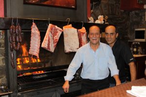 Due uomini davanti a carne appesa su griglia.