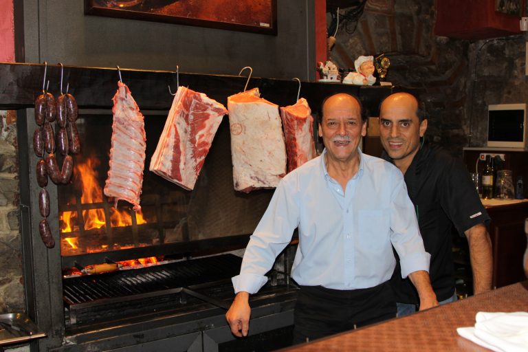 Due uomini davanti a carne appesa su griglia.