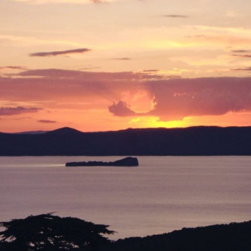 Tramonto su lago con isola e cielo colorato.